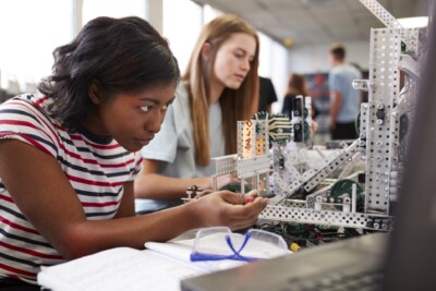 Two Female College Students Building Machine In Science Robotics Or Engineering Class